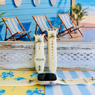 Palm Shore Club silicone Apple Watch band with hand-painted palm trees over soft blue and yellow cabana stripes on an ivory base, shown displayed and worn on Apple Watch against a coastal beach club backdrop.
