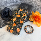 Haunted Blossoms MagSafe grip ring lying beside the matching black gothic floral Wavy Luxe case on black spiderweb mesh.