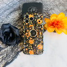 Haunted Blossoms MagSafe grip ring attached to the matching black coral rose Wavy Luxe case, styled with a black rose and an orange bloom.