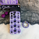 Ghostly Whisker's MagSafe grip ring lying beside the matching lavender ghost and cat Wavy Luxe case with purple glitter pumpkins.