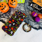 Spooky MagSafe grip ring lying beside the matching Wavy Luxe case, showing the black pumpkin and skull print on both.
