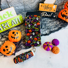 Spooky scrunchie phone wrist strap and matching Wavy Luxe case styled together with a Hey Boo sign and orange jack-o-lantern pails.