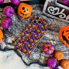Jack-O-Lantern Jive Wavy Luxe MagSafe iPhone case laid flat on black spiderweb mesh with orange jack-o-lantern pails and glitter pumpkins.