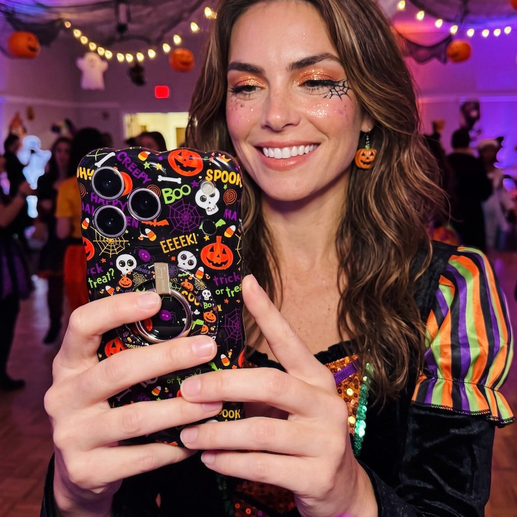 Woman holding the Spooky Wavy Luxe MagSafe iPhone case at an indoor Halloween party strung with lights.