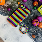 Main Witch Energy MagSafe grip ring lying beside the matching striped Wavy Luxe case, showing the black, purple, green and orange stripes on both.