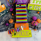 Main Witch Energy scrunchie phone wrist strap and matching striped Wavy Luxe case shown together on a Hocus Pocus sign.