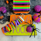 Main Witch Energy scrunchie phone wrist strap on a Trick or Treat board with a large black spider prop and glitter pumpkins.