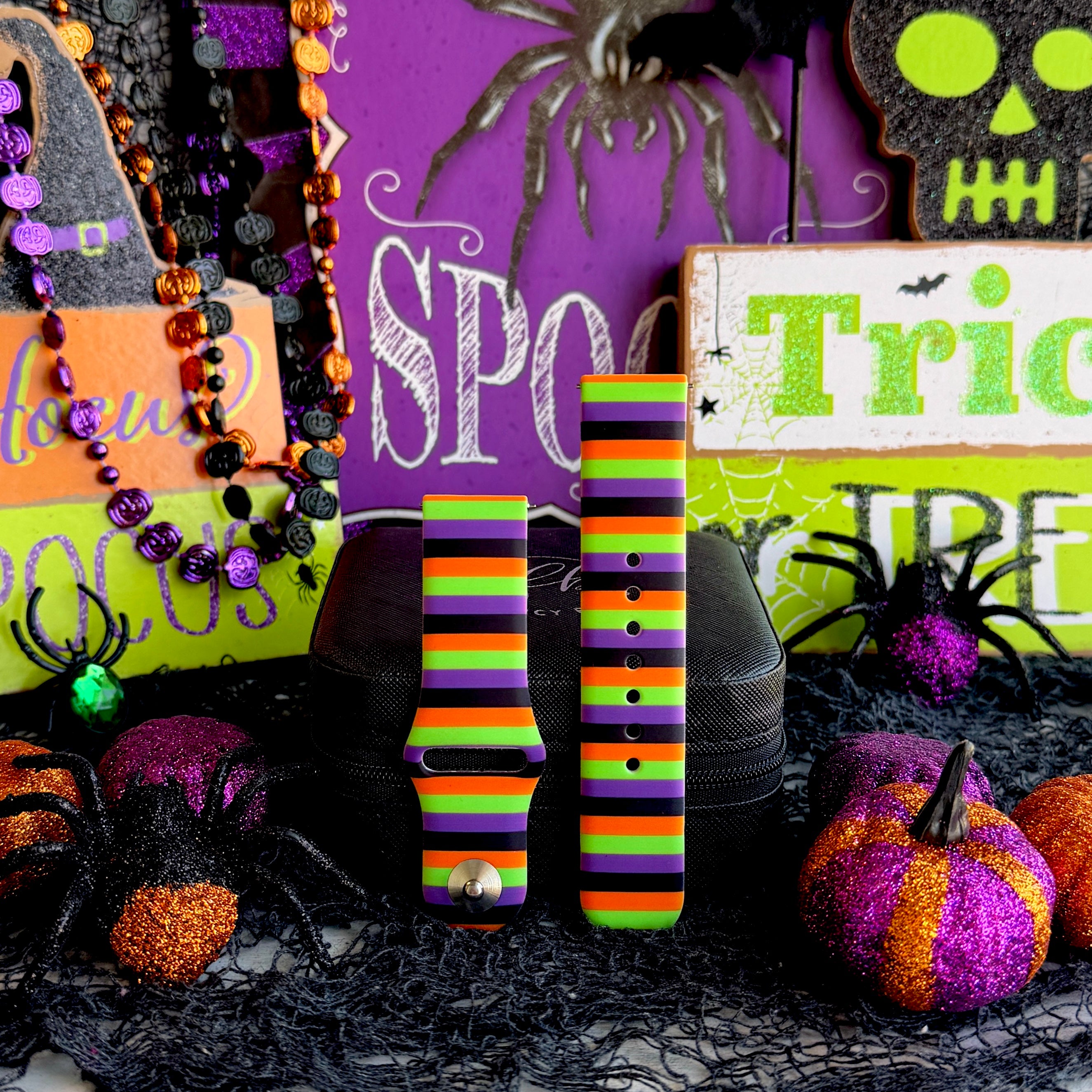 Two Main Witch Energy Samsung Galaxy Watch band straps standing side by side with black spider props and glitter pumpkins.