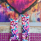 Love Out Loud silicone Apple Watch band with hand-drawn graffiti-style hearts in pink, magenta, blue, teal, red, and black on a white base, shown displayed and worn on Apple Watch against a colorful street art backdrop.
