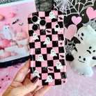 Hand holding the Hey Boo, Looking Cute Wavy Luxe MagSafe iPhone case, pink and black checkerboard with white ghosts, black bats and white spiderwebs.