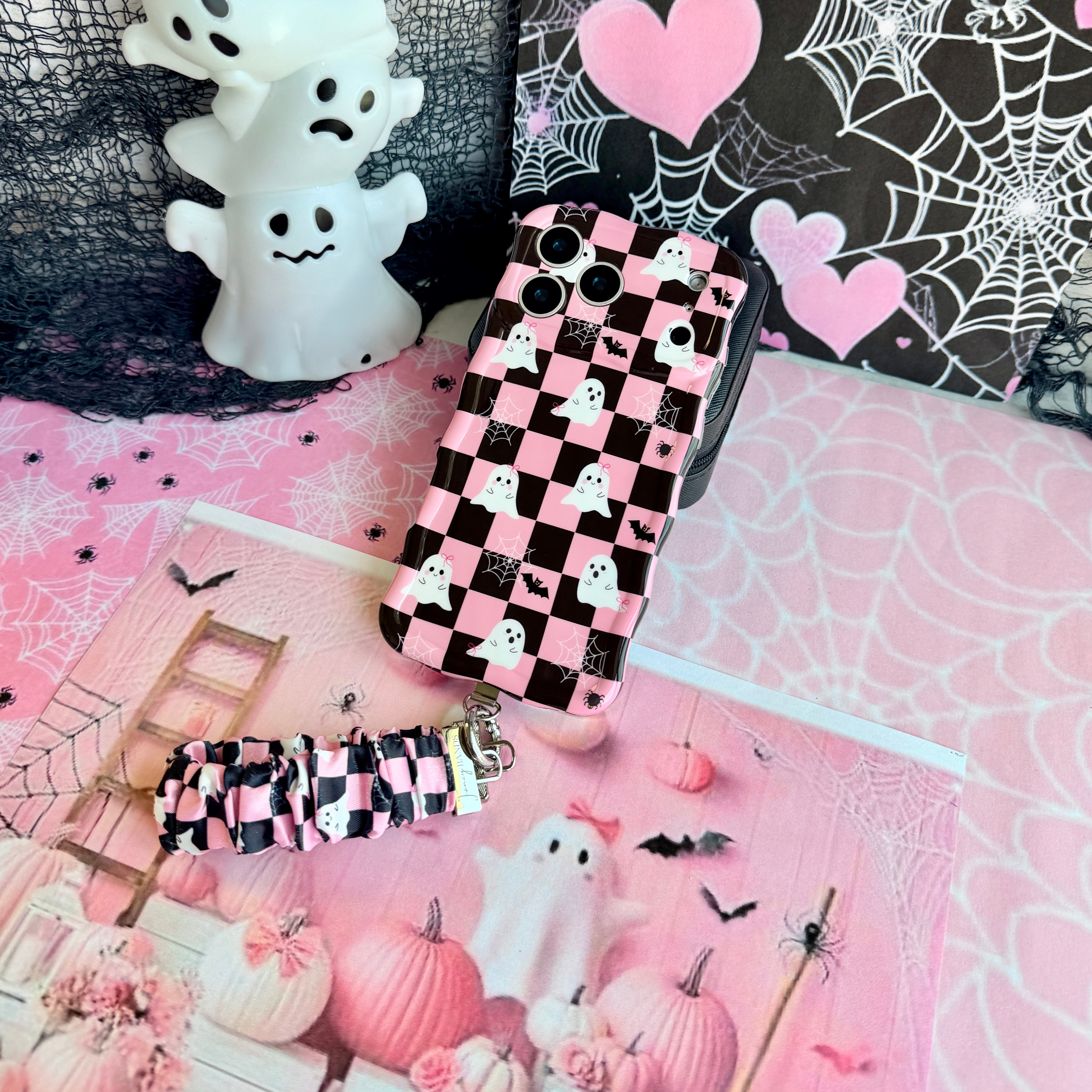 Hey Boo, Looking Cute scrunchie phone wrist strap in pink and black checkerboard, clipped to the matching ghost print iPhone case