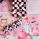 The Hey Boo, Looking Cute Scrunchie Phone Wrist Strap clipped to the matching pink and black checkerboard ghost phone case, hanging from the metal clasp.
