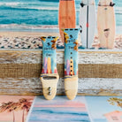 Sweet Summer silicone Apple Watch band with pastel pink, yellow, and blue surfboards, palm trees, and "sweet summer time" script on a soft watercolor beach scene, shown displayed and worn on Apple Watch against a coastal surfboard backdrop.