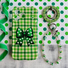 Green and white gingham check Wavy Luxe phone case with a large green bow and heart pattern, paired with an iridescent and emerald beaded 'Bow & Bling' phone wrist strap.