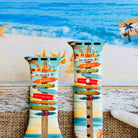 Seaside State of Mind silicone Apple Watch band with colorful surfboard signpost on a beach scene and "Be Crazy, Be Silly, Be Weird—life is too short to be anything but happy" message, shown displayed and worn on Apple Watch against a beach backdrop.
