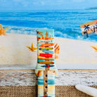 Seaside State of Mind silicone Samsung Watch band with colorful surfboard signpost on a beach scene and "Be Crazy, Be Silly, Be Weird—life is too short to be anything but happy" message, shown displayed and worn on Apple Watch against a beach backdrop.