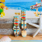 Seaside State of Mind silicone Samsung Watch band with colorful surfboard signpost on a beach scene and "Be Crazy, Be Silly, Be Weird—life is too short to be anything but happy" message, shown displayed and worn on Apple Watch against a beach backdrop.