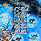 The Bewitching Hour Wavy Luxe MagSafe iPhone case lying flat with the matching MagSafe grip ring attached, on a moonlit blue Halloween backdrop.