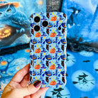 Hand holding The Bewitching Hour Wavy Luxe MagSafe iPhone case, light blue with orange and blue jack-o-lanterns, blue witch hats, owls and yellow crescent moons.