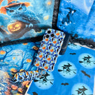 The Bewitching Hour Scrunchie Phone Wrist Strap and matching light blue witch print phone case laid out together on a moonlit Halloween backdrop.