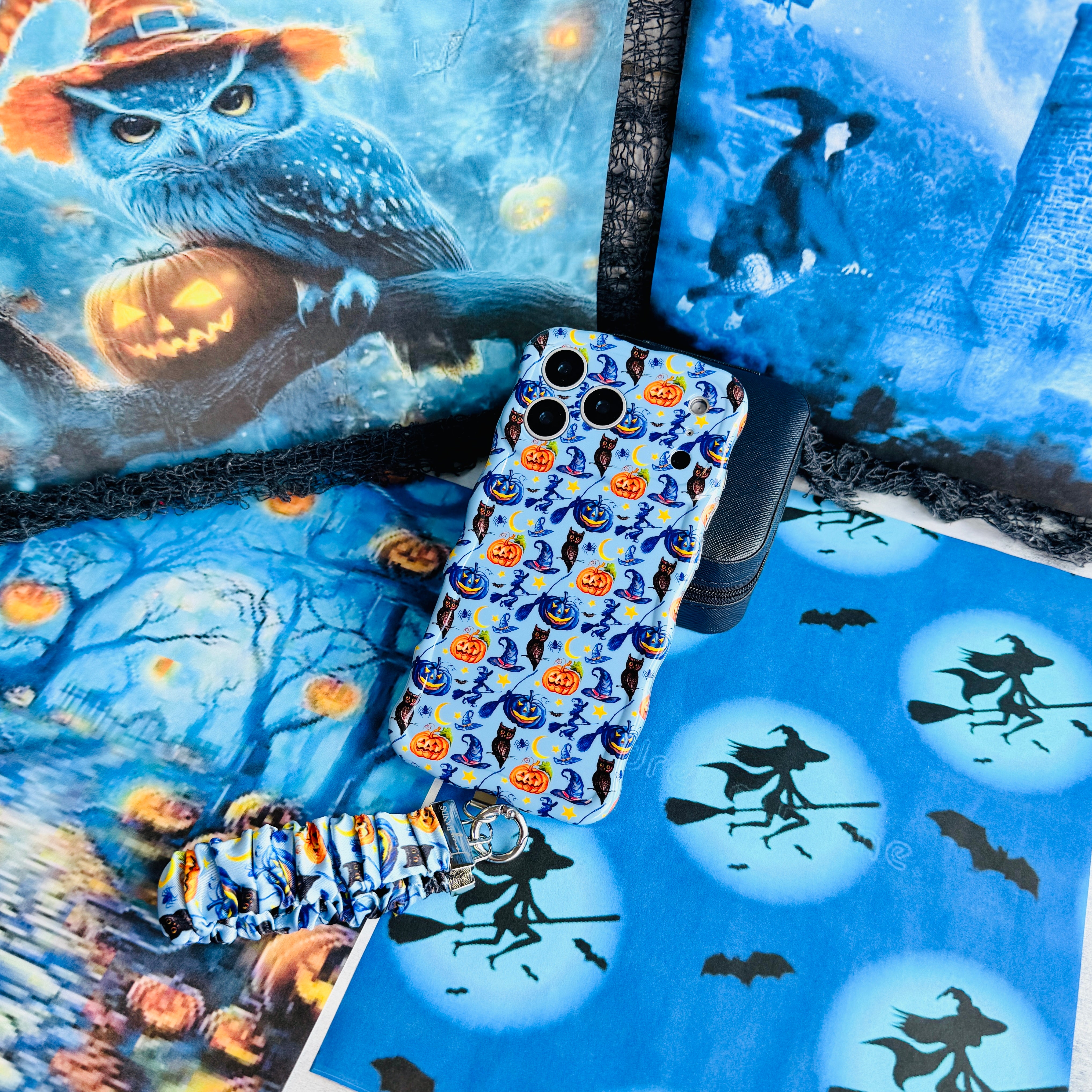 The Bewitching Hour Scrunchie Phone Wrist Strap and matching light blue witch print phone case laid out together on a moonlit Halloween backdrop.