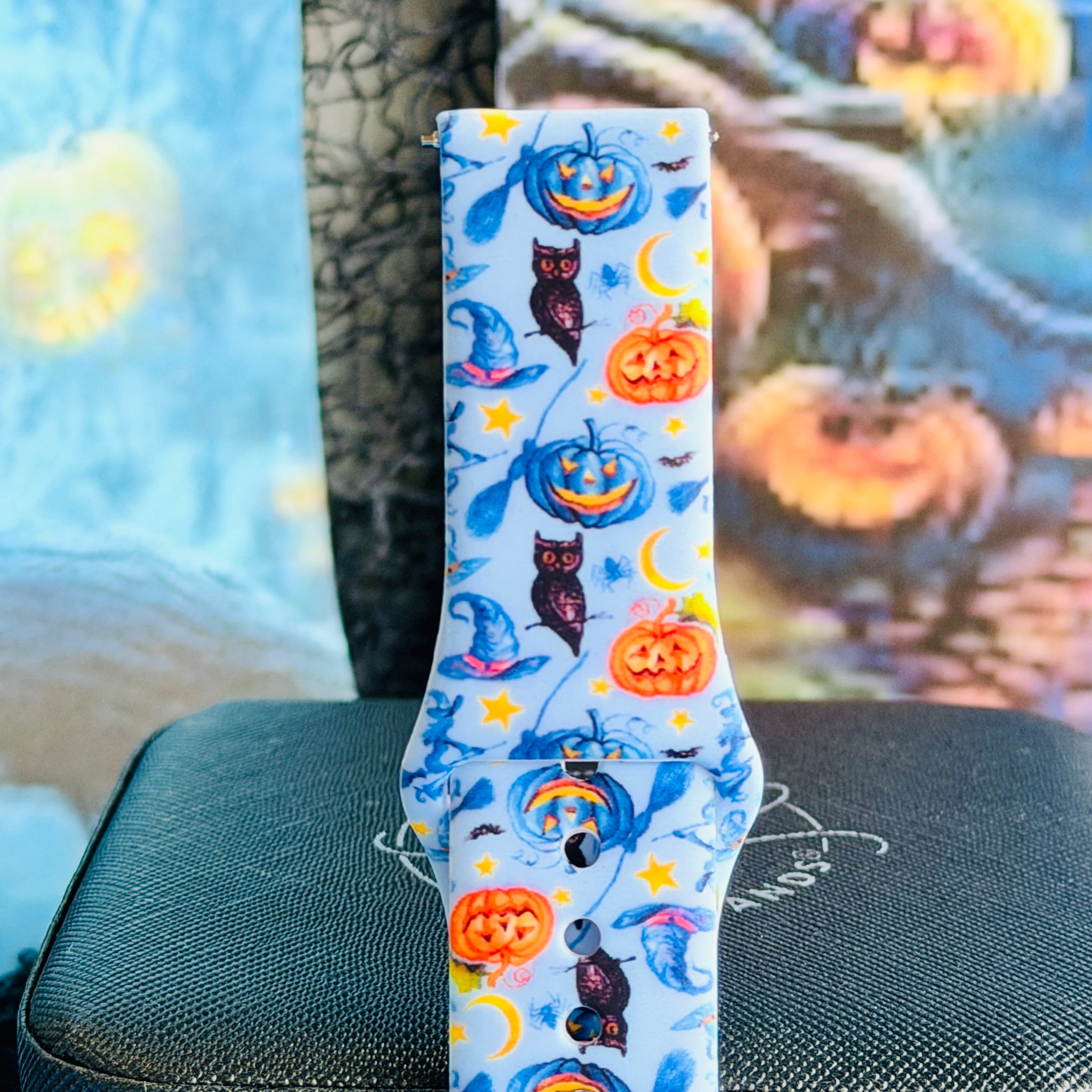 Close view of The Bewitching Hour Samsung Galaxy Watch band showing orange and blue jack-o-lanterns, owls, yellow stars and crescent moons on light blue silicone.