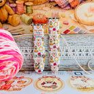 It's Giving Grandma Hobbies silicone Apple Watch band with "hot girls have grandma hobbies" script, patchwork hearts, yarn balls, knitting needles, embroidery hoops, lanterns, pies, and teacups on a cream base, shown displayed and worn on Apple Watch against a cottagecore craft backdrop.