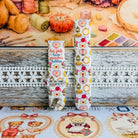 It's Giving Grandma Hobbies silicone Samsung Galaxy Watch band with "hot girls have grandma hobbies" script, patchwork hearts, yarn balls, knitting needles, embroidery hoops, lanterns, pies, and teacups on a cream base, shown displayed and worn against a cottagecore craft backdrop.