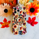 Sienna Petals Hold It Fancy MagSafe grip ring attached to the matching cream rust floral iPhone case, styled with sunflowers and a knit pumpkin.