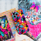 Trendy wavy iPhone case featuring a vibrant street-art collage of electric blue and yellow butterflies over neon pink paint splatters with a high-gloss finish.