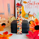 Sienna Petals silicone Apple Watch band standing full length in front of a Gather Together fall sign with pumpkins and autumn leaves.