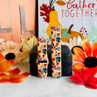 Sienna Petals Samsung Galaxy Watch band shown in both size options on a black stand against an autumn leaf and sunflower backdrop.