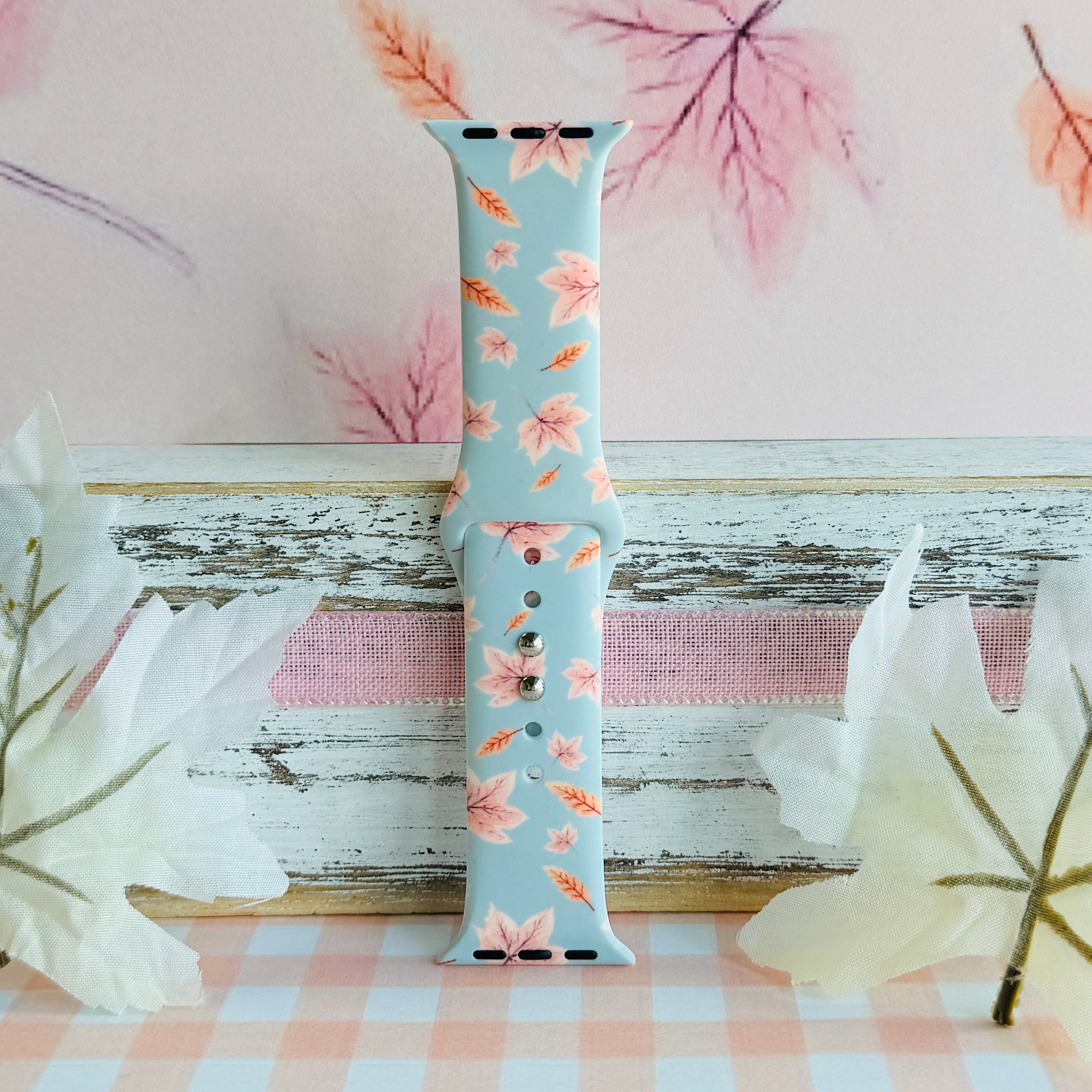 Autumn Breeze silicone Apple Watch band standing full length against a soft pink backdrop painted with maple leaves.