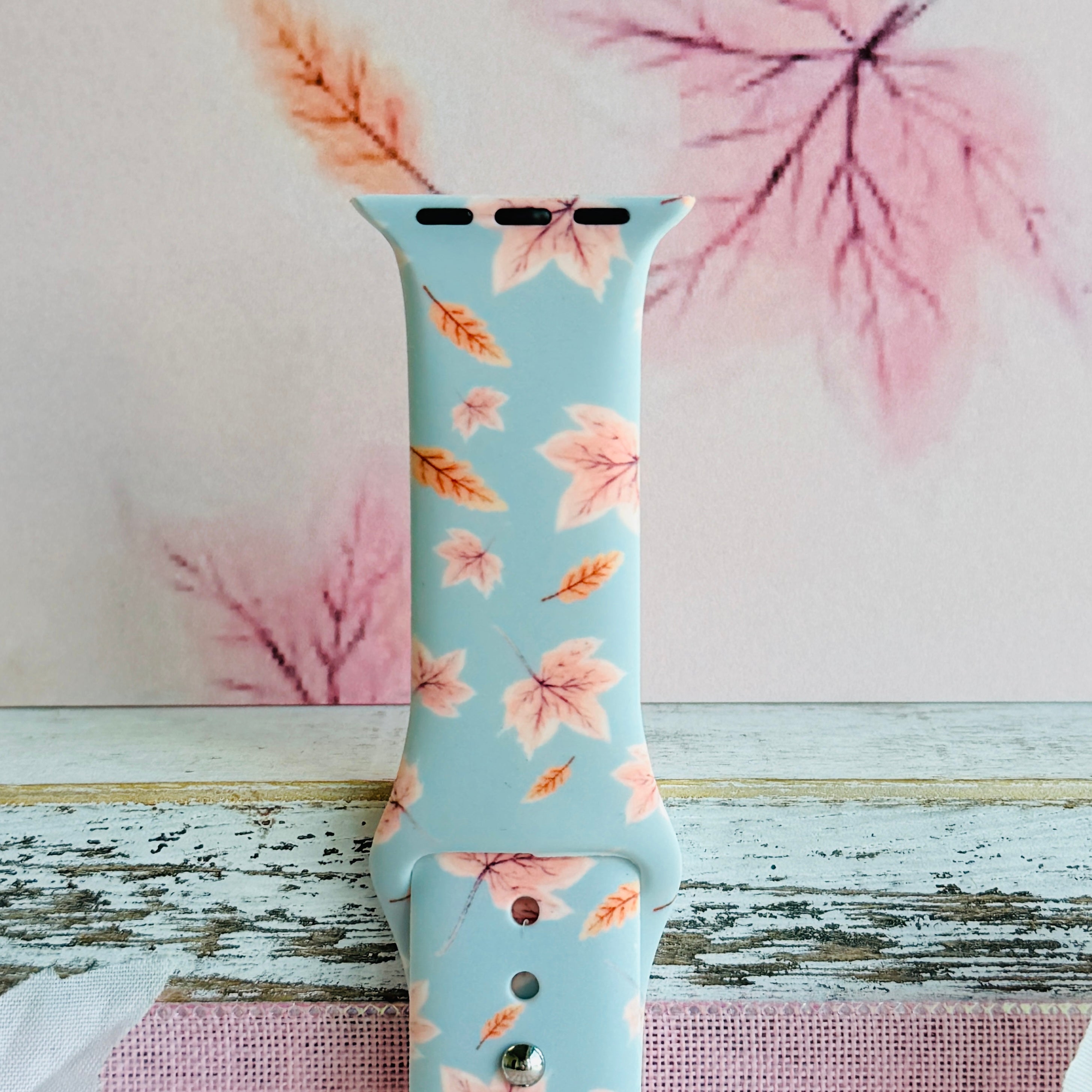 Close view of the Autumn Breeze Apple Watch band showing the coral wheat sprigs and blush maple leaves on dusty blue silicone.