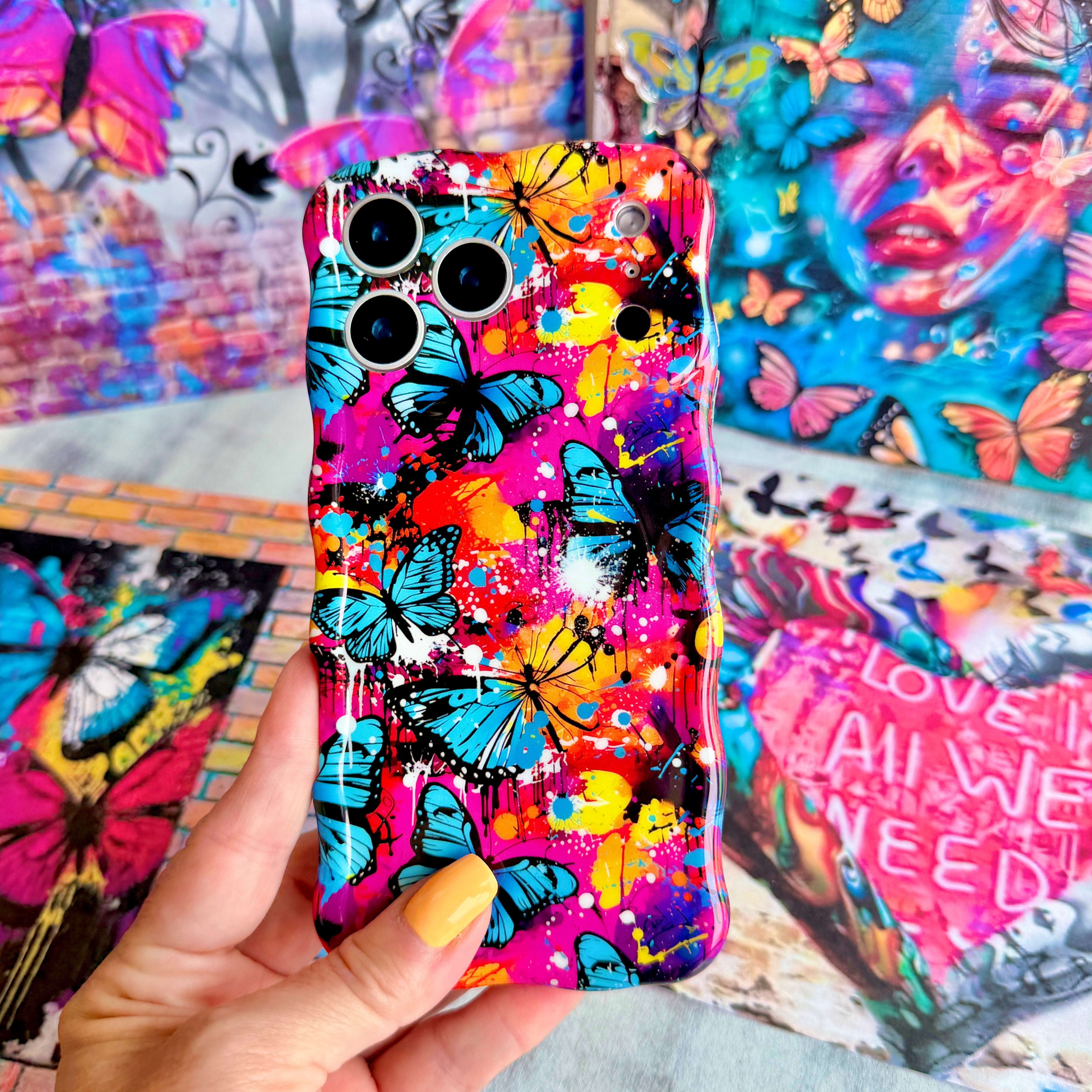 Trendy wavy iPhone case featuring a vibrant street-art collage of electric blue and yellow butterflies over neon pink paint splatters with a high-gloss finish.