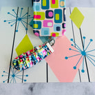 Mod Mood Scrunchie Phone Wrist Strap clipped to the matching retro geometric phone case, on an atomic starburst backdrop.