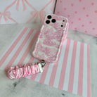 Blush Manor Wavy Luxe phone case standing with the matching pink toile scrunchie wrist strap, against a pink stripe and bow backdrop.