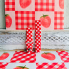 Red Barn Babe Samsung Galaxy Watch band in both size options on a whitewashed wood ledge with a red gingham picnic cloth.