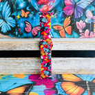 Rebel Wings silicone Apple Watch band with graffiti-style butterflies in blue, orange, yellow, and white over a hot pink and magenta paint-splatter background, shown displayed and worn on Apple Watch against a colorful street art butterfly backdrop.