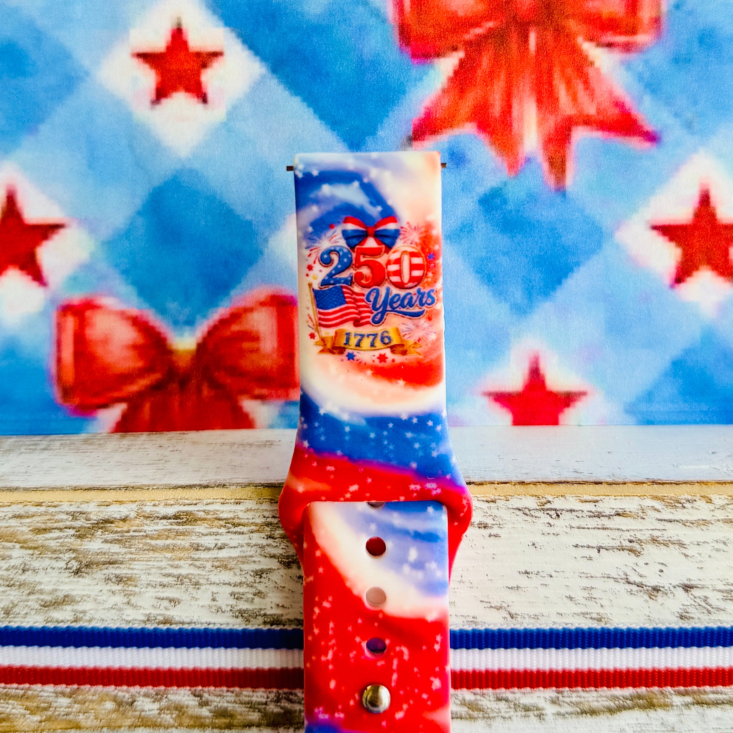 Sweet Freedom 250 silicone Samsung Galaxy Watch band celebrating America's 250th anniversary with "250 Years 1776" emblem, American flag, fireworks, red bow, and red, white, and blue tie-dye swirl with star sparkle, shown displayed and worn against a patriotic 4th of July backdrop.