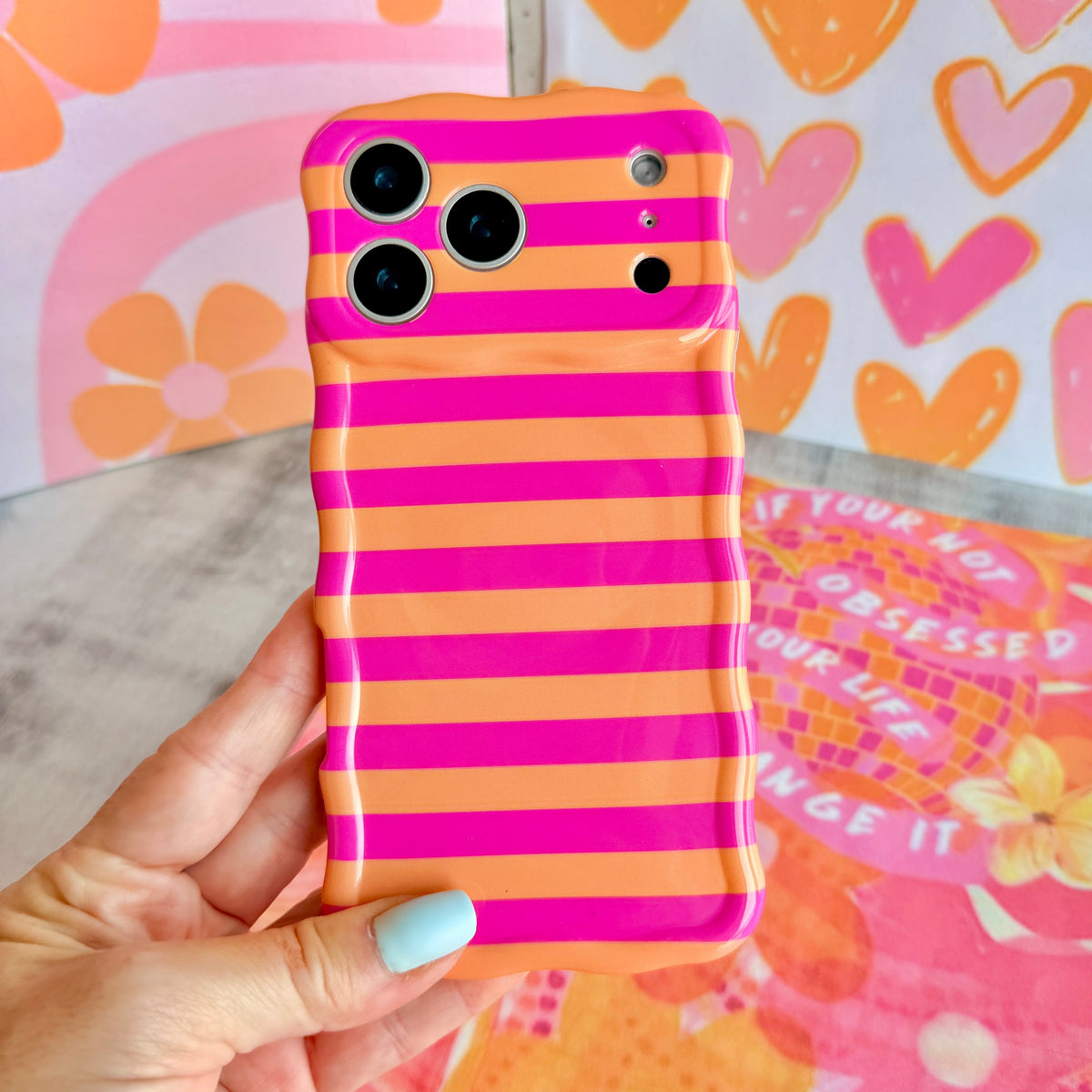 Hand holding the Candy Citrus Stripes Wavy Luxe MagSafe iPhone case, bold hot pink and orange cabana stripes