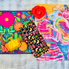 Trendy black wavy iPhone case featuring an intricate folk art botanical pattern of red flowers, magenta details, and yellow fan petals with a high-gloss finish.