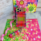 Hazy Tartan scrunchie phone wrist strap laid flat beside the matching blurred rainbow plaid phone case on a bright daisy print background.