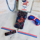 USA Fireworks scrunchie phone wrist strap laid flat with the matching firework phone case, star-spangled sunglasses and a red, white and blue beaded strand.