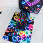 Neon Taffy scrunchie phone wrist strap laid flat next to the matching neon swirl phone case on a bright neon heart print background.
