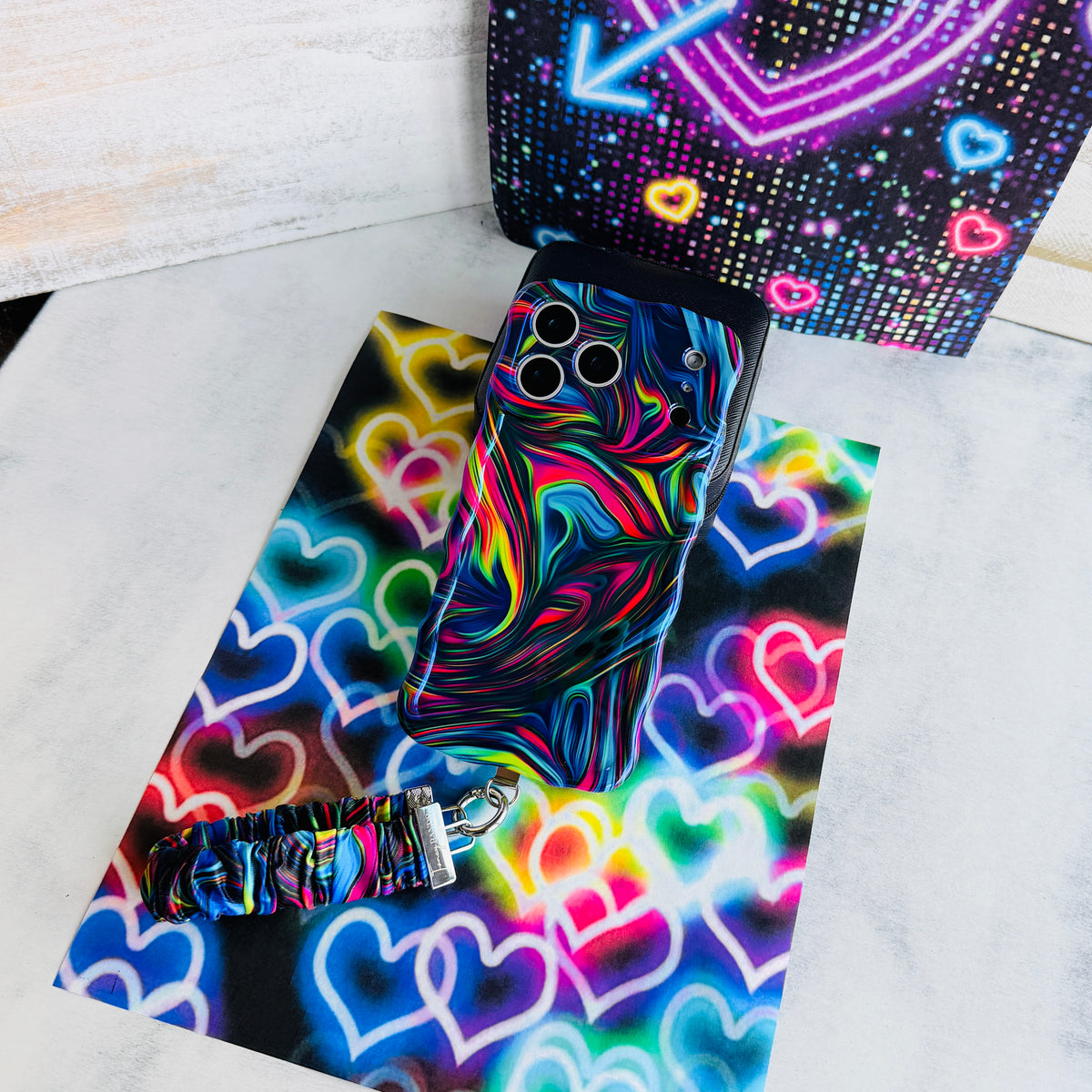 Neon Taffy scrunchie phone wrist strap laid flat next to the matching neon swirl phone case on a bright neon heart print background.