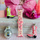 Pink watch strap with cowboy boot design, surrounded by decorative items on a wooden surface.