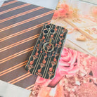Pretty Little Details black pearl and rose iPhone case wearing the matching MagSafe grip ring, styled on striped paper with pink rose prints.