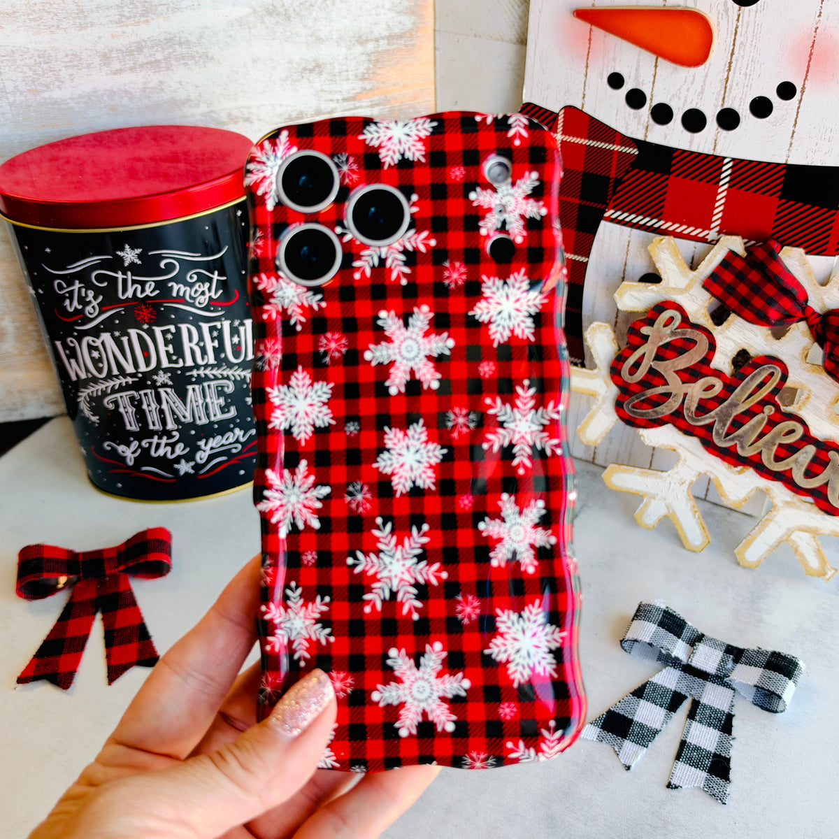 Hand holding the Buffalo Plaid Snowflake Wavy Luxe MagSafe iPhone case, red and black buffalo check scattered with white snowflakes
