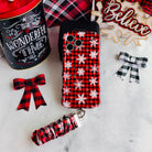 Buffalo Plaid Snowflake iPhone case with the matching scrunchie phone wrist strap attached, laid flat with a Believe sign and buffalo check bows